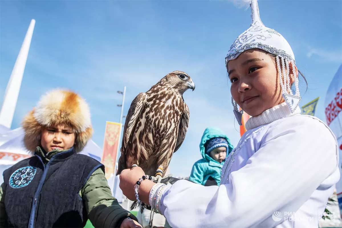Девочка в национальном костюме держит сокола во время празднования Навруза на территории 